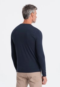 Pitkähihaisen tummansinisen paidan pehmeä kankaasta, jossa on pyöreä kaula-auko ja istuva muotoilu, saumattomilla olkasaumoilla ja siistillä viimeistelyllä.