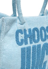 Blå handdukstygs tote bag med mjuk textur, med präglad text i en mörkare blå som säger "VÄLJ JUICE." Handtagen är rejäl och loopade.