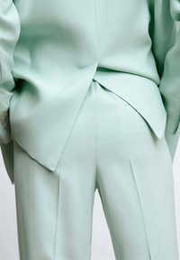Mintgroen op maat gemaakt pak met een gestructureerde blazer met een enkele split en bijpassende hoge taille broek, beide gemaakt van een gladde stof.