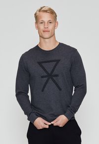 Camisa de manga larga gris oscuro hecha de una tela suave, con un diseño gráfico negro texturizado en el centro. Se ajusta cómodamente alrededor del escote.
