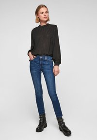 Blusa negra de manga larga con rayas sutiles, combinada con jeans ajustados azules y botas negras hasta el tobillo con herrajes decorativos.