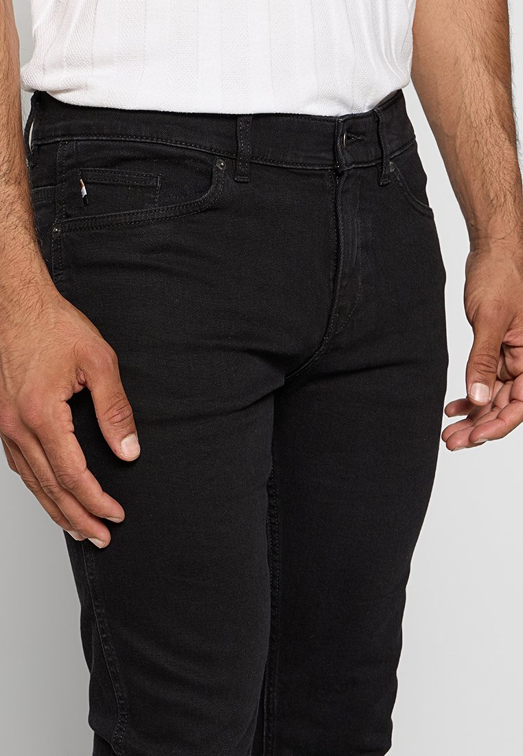Jean noir en denim avec une coupe ajustée, comportant une poche avant, des passants de ceinture et des coutures contrastées. Texture douce avec un léger extensibilité.