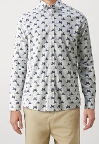 Koszula zapinana na guziki z lekkiego materiału o białej bazie, ozdobiona rozproszonym granatowym abstrakcyjnym wzorem. Długie rękawy i standardowy kołnierz.