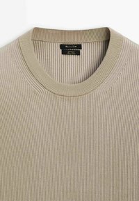 Beige geripptes Strick-Sweatshirt mit schmalem Kragen und einem schwarzen Markenetikett, das im Halsausschnitt eingenäht ist.