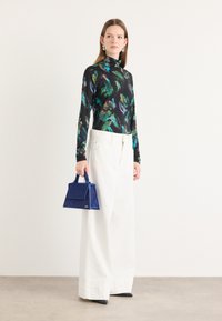 Top negru cu maneci lungi, cu imprimeu floral verde și albastru, asortat cu pantaloni albi cu picioare largi. Ține o geantă mică albastră, cu o formă bine definită.
