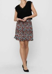 Černý top s krajkovým lemováním a výstřihem do V, doplněný rozšířenou květinovou sukní s červenými, modrými a bílými vzory. Nosené s černými podpatky.