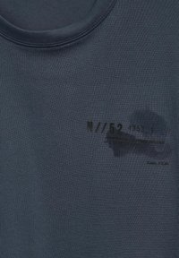 Tmavě modré tričko vyrobené z bavlny s kulatým výstřihem. Obsahuje černý potisk textu a rozmazaný detail, bez viditelných vzorů nebo akcentů.