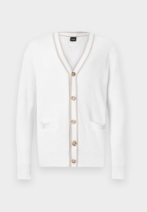 Beli pleteni pulover z V-izrezom z rjavim robom, petimi rjavimi gumbi in dvema sprednjima žepoma, prikazan na običajni podlagi.