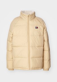 Chaqueta de abrigo en beige claro con alto cuello, cremallera completa, textura acolchada, puños elásticos y pequeño parche de marca en el pecho.
