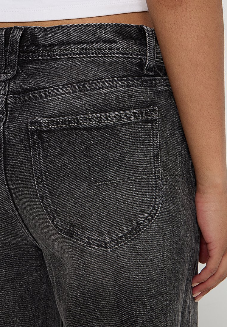 Jeans in denim nero sbiadito con vita alta, grandi tasche posteriori e dettagli di cucitura visibili. Presentano un tessuto testurizzato e un leggero usura.