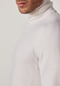 Maglione bianco a collo alto con un design aderente, texture a coste sul colletto e tessuto morbido. Dettaglio in prima persona che mette in risalto l'area del collo.