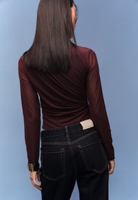 Viininpunainen pitkähiha paita, joka on valmistettu läpikuultavasta materiaalista, yhdistetty tummiin farkkuihin. Huomionarvoisia yksityiskohtia ovat sileä pinta ja istuva malli.