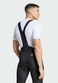 Schwarze Fahrradbib-Shorts mit gepolstertem Sitz, kombiniert mit einem weißen, figurbetonten Oberteil. Verfügt über verstellbare schwarze Träger für einen sicheren Sitz.