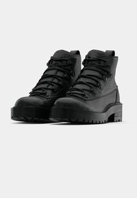 Stivaletti da trekking neri con tomaia in pelle testurizzata, punta tonda, chiusura frontale con lacci e suola spessa e robusta per una migliore trazione.