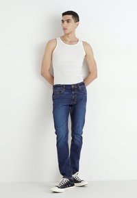 Blå denimjeans med slim fit, som har fem lommer og glidelås. Kombinert med en hvit tank topp og svarte sneakers.
