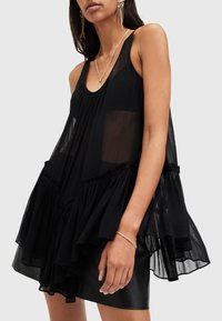 Black sheer sleeveless top with gathered fabric and ruffled hem. Lightweight material with a flowy design and a round neckline.