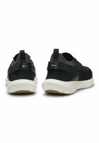 Chaussures de sport noires avec une tige en mesh texturé, des accents noirs lisses, des semelles blanches et une semelle extérieure en caoutchouc plate. Détails réfléchissants au niveau du talon.