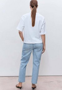 Camiseta blanca de manga corta combinada con unos jeans rectos de color azul claro. La camiseta tiene un corte holgado; los jeans cuentan con bolsillos estándar y un corte clásico.