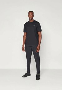 Svart idrottströja och byxor, kort ärm, rund hals, mjuk textur, slim fit, accentuerad med en liten logotyp på bröstet.