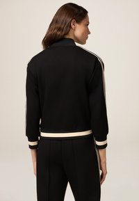 Sweatshirt cropped nero con collo e polsini a costine, caratterizzato da righe bianche ai lati. Tessuto liscio, design minimal.