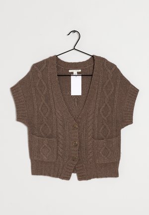 Brązowy krótki sweter na guziki z dzianiną w warkocz, trzy guziki, dwie przednie kieszenie oraz dekolt w serek, zawieszony na czarnym wieszaku na białym tle.