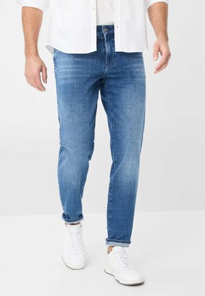 Jeans in denim azzurro chiaro con taglio affusolato, caratterizzati da un leggero effetto scolorito, design a cinque tasche e orli arrotolati, abbinati a sneakers bianche.