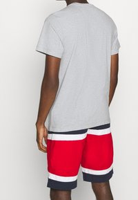 Šedé bavlněné tričko s krátkým rukávem, v kombinaci s červenými plavkovými šortkami s bílými a námořnickými pruhy na lemu a pase.