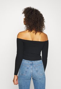 Svart, off-shoulder, ribbad långärmad topp i kombination med högmidjade, ljusblå jeans, som visar en figursydd design och synlig sömnad.