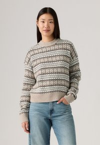 Gebreide trui in beige met patroonbanden van bruine en witte diamanten, ronde halslijn, geribde manchetten en zoom. Gecombineerd met lichtblauwe jeans.
