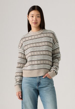 Gebreide trui in beige met patroonbanden van bruine en witte diamanten, ronde halslijn, geribde manchetten en zoom. Gecombineerd met lichtblauwe jeans.