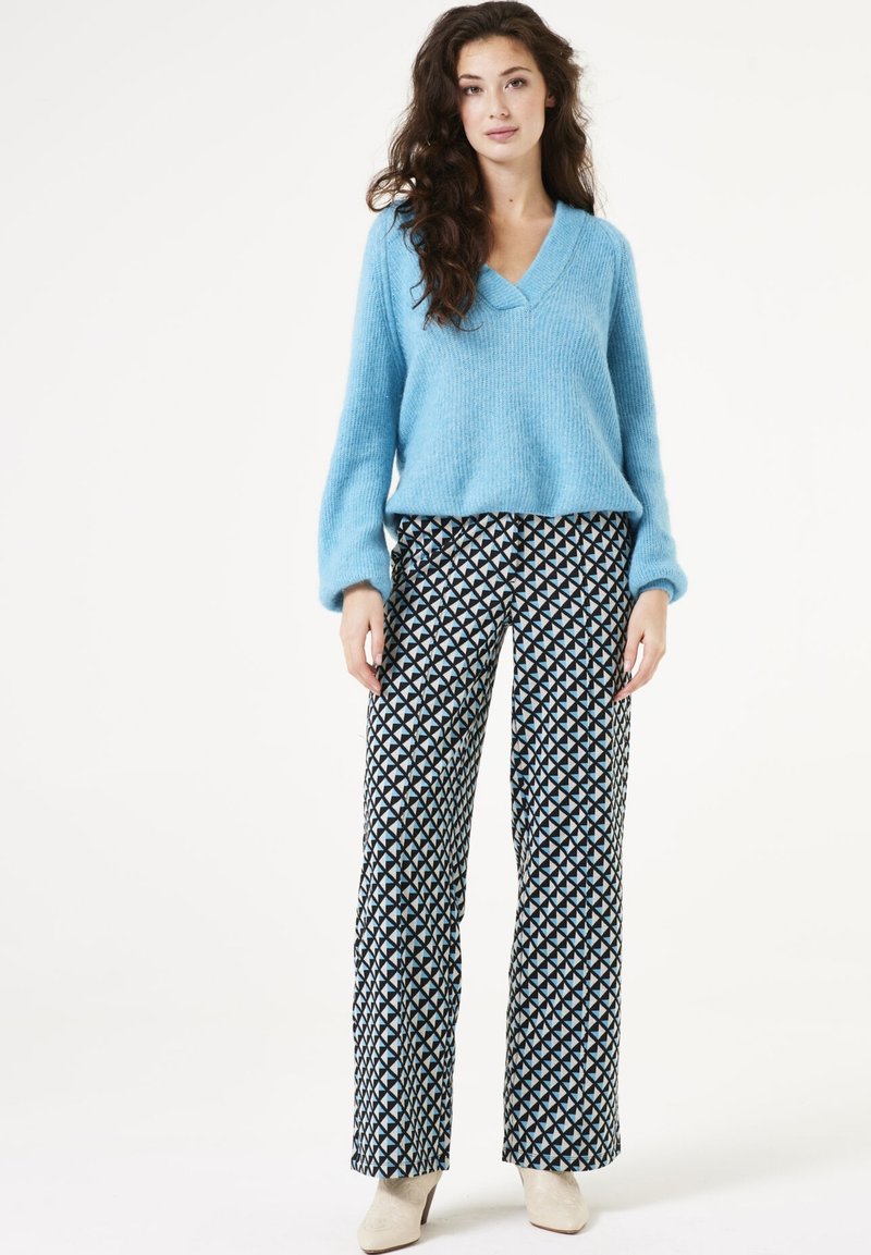 Lichtblauwe gebreide trui met een V-hals ontwerp, gecombineerd met gestreepte zwart-witte brede broek met een geometrische print.