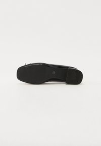 Chaussure en cuir noire vue du côté de la semelle, avec un bout carré et un talon texturé marqué "ANTI SLIDE" sur fond blanc.