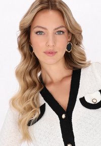 Cardigan bianco a maglia con dettagli neri, caratterizzato da un profondo scollo a V, due tasche applicate e bottoni dorati. Texture morbida e design leggero.
