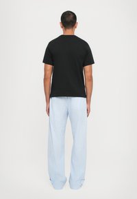 Schwarzes Baumwoll-T-Shirt mit kurzen Ärmeln, kombiniert mit hellblau-weiß gestreiften Schlafanzughosen mit lockerer Passform und Knopfakzenten.