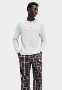 Light gray long-sleeve henley shirt with three buttons, paired with multicolored plaid pants featuring navy, brown, and orange tones.