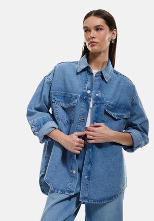 Helles blaues Denim-Hemd mit Kragen, Knopfverschluss, zwei Brusttaschen und aufgerollten Ärmeln. Lässiger Schnitt mit gesteppten Details und abgerundetem Saum.