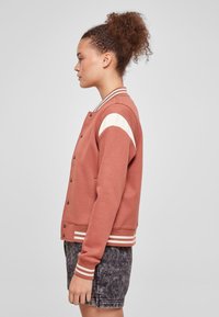 Pehmeast kangast roostevärvi bomber-jakk, millel on varrukaõmblustel valged triibud ja soonikkätised, kinnitatav trukiga ja küljetaskutega.