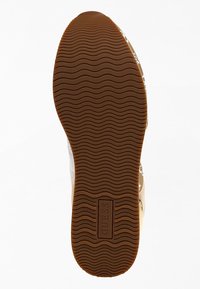 Semelle de chaussure en caoutchouc marron avec un motif ondulé et le logo "GUESS" embossé au centre sur un fond blanc.