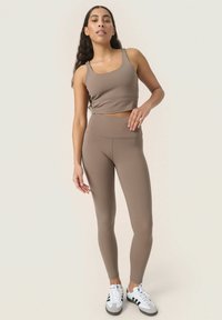 Barna, rövidített tank top, amelyhez illeszkedő, magas derekú leggings tartozik, puha, rugalmas anyagból készült. A sportcipők fekete csíkokkal és fehér alappal rendelkeznek.