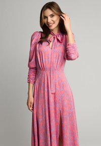 Maxi sukienka w różowym i lawendowym kolorze z kwiatowym wzorem, posiadająca długie bufiaste rękawy, związany dekolt oraz rozcięcie z przodu. Wykonana z lekkiego materiału.