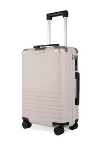 Krämfarbener Hartschalenkoffer mit gerippter Textur, ausziehbarem Griff, schwarzen Rädern und silbernen Akzenten. Ausgestattet mit einem Zahlenschloss.