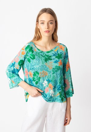 Lightweight, turquoise floral top featuring green, orange, and pink patterns, round neckline, and three-quarter sleeves, paired with white pants.