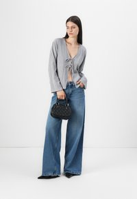 Gray striped top with tie-front detail, wide-leg blue jeans, and a small black textured handbag. Model stands against a plain background.