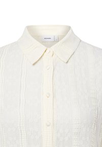 Weißes, strukturiertes Hemd mit Kragen, das vertikale Streifen und Knopfverschlüsse aufweist. Etikett im Kragen angebracht.