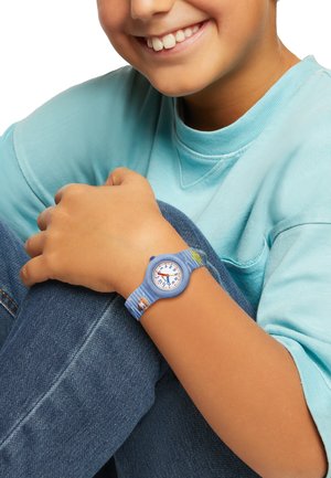Montre pour enfants bleue avec un bracelet en silicone rayé, un cadran rond et des index heures blancs. Accents de dessins animés importants sur le bracelet.