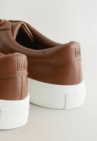 Ruske nahkatekenjake s nizkim profilom, belim gumijastim podplatom, teksturiranim naglasbcima in detajlom logotipa na peti.