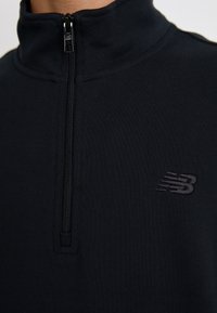 Sudadera negra de media cremallera en un tejido suave y elástico. Presenta un cuello elevado y un pequeño logo bordado en el pecho.
