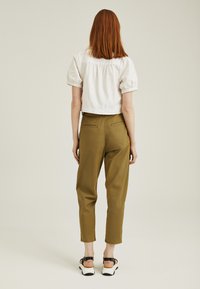 Blusa blanca corta con mangas abullonadas combinada con pantalones tapered verdes oliva. Sandalias negras y beiges completan el conjunto.