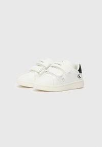 Baskets sportives blanches pour enfants avec deux bandes Velcro, tige en synthétique lisse, renforcement au talon noir et perforations subtiles pour la respirabilité.
