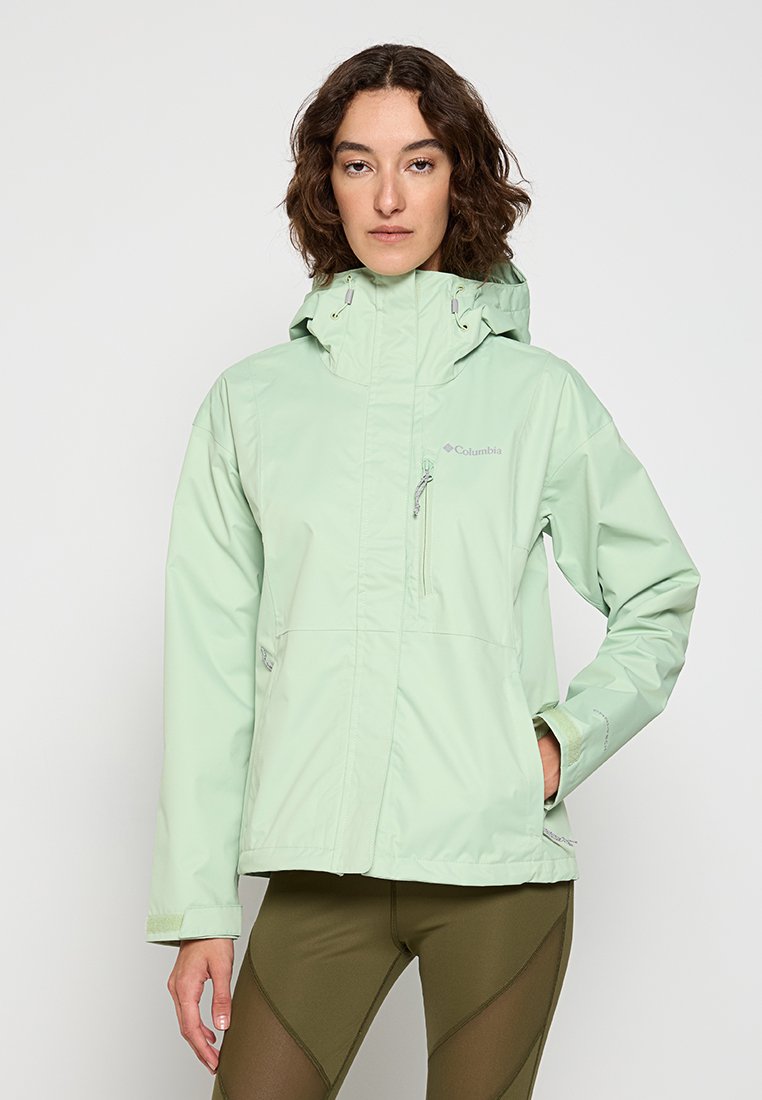 Veste imperméable vert clair avec capuche, poches zippées et texture lisse. Présente un logo sur la poitrine et des poignets ajustables.